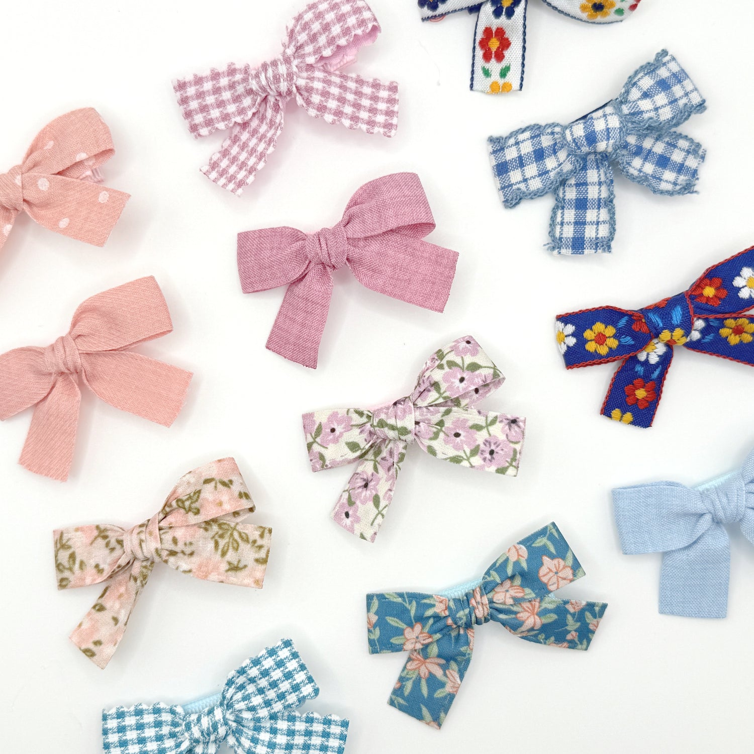 A collection of hair bow clips in various shades of pink and blue, with different patterns such as solid color, gingham, floral, and striped.